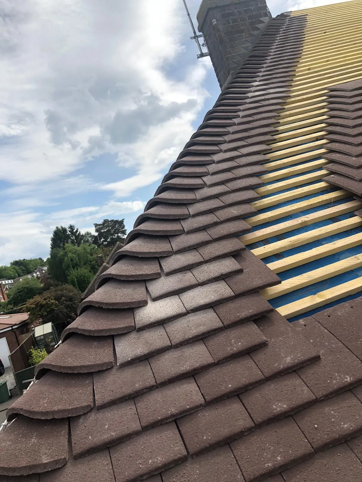 A section of a residential roof in the process of being re-tiled, showing new brown tiles next to exposed roof battens and underlayment.