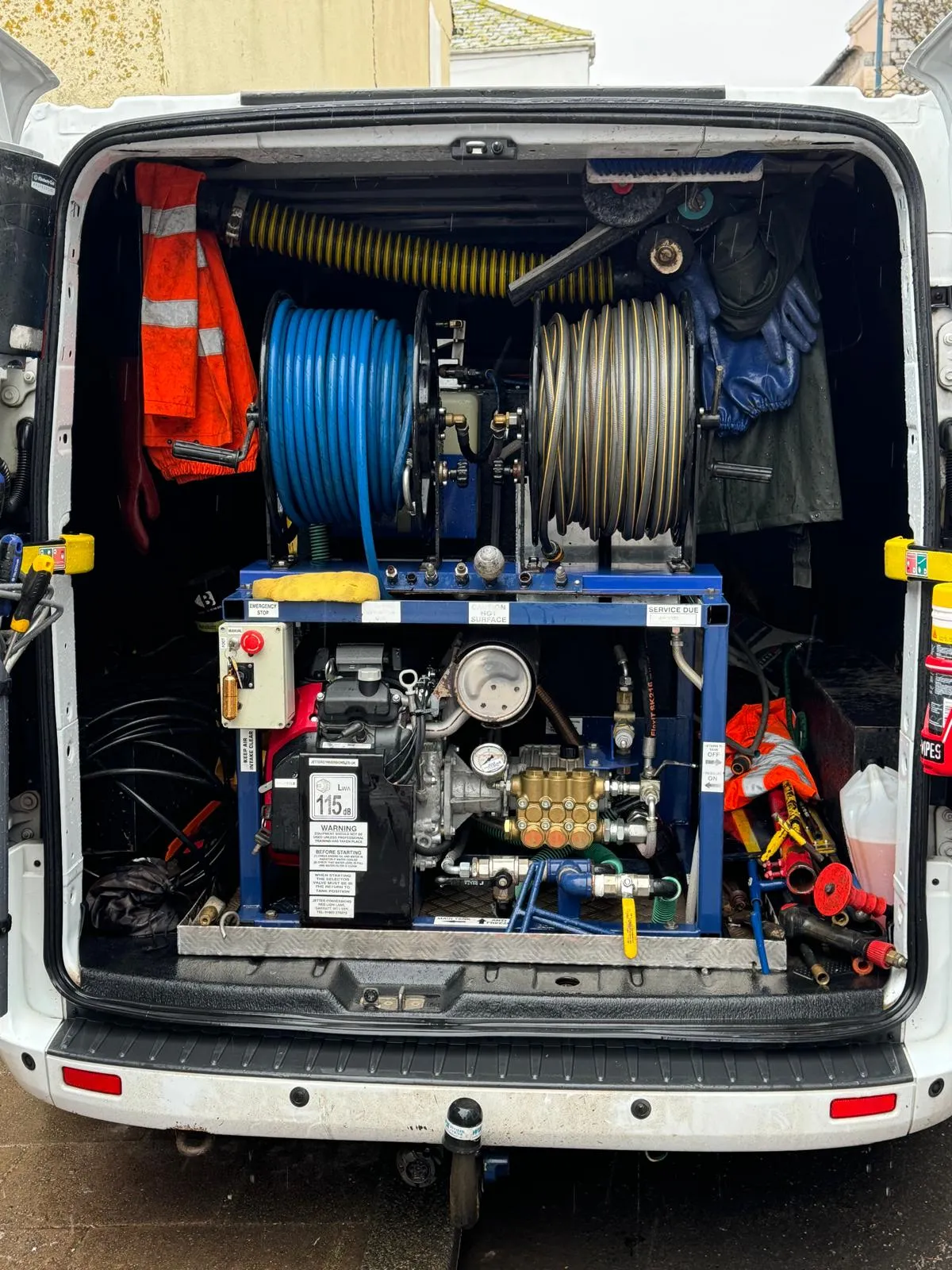 Rear view of a drainage service van showing high-pressure water jetting equipment, hose reels, and safety gear, ready for unblocking drains.