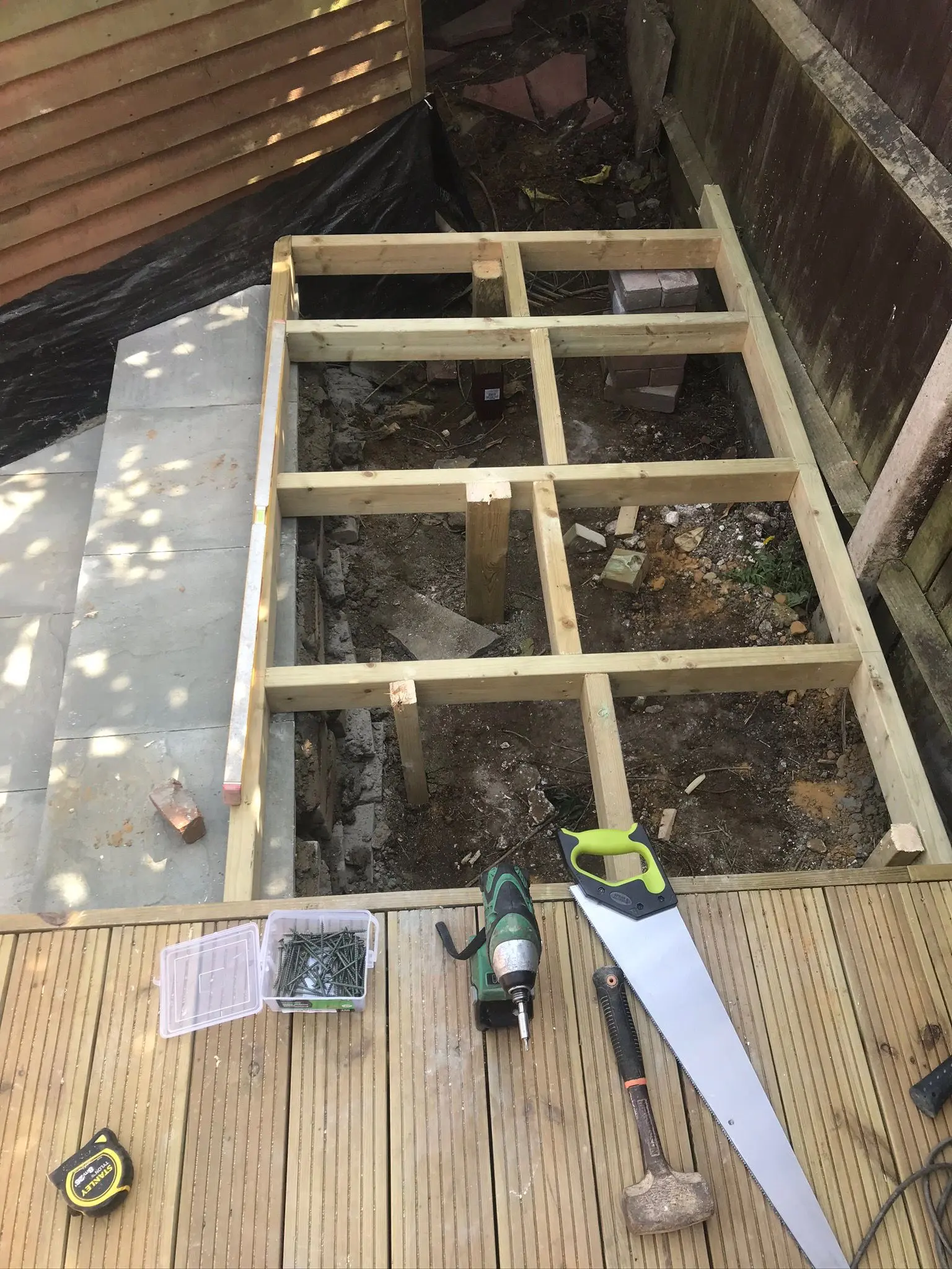 Timber framework under construction for a base or decking area, showing site preparation and various hand tools