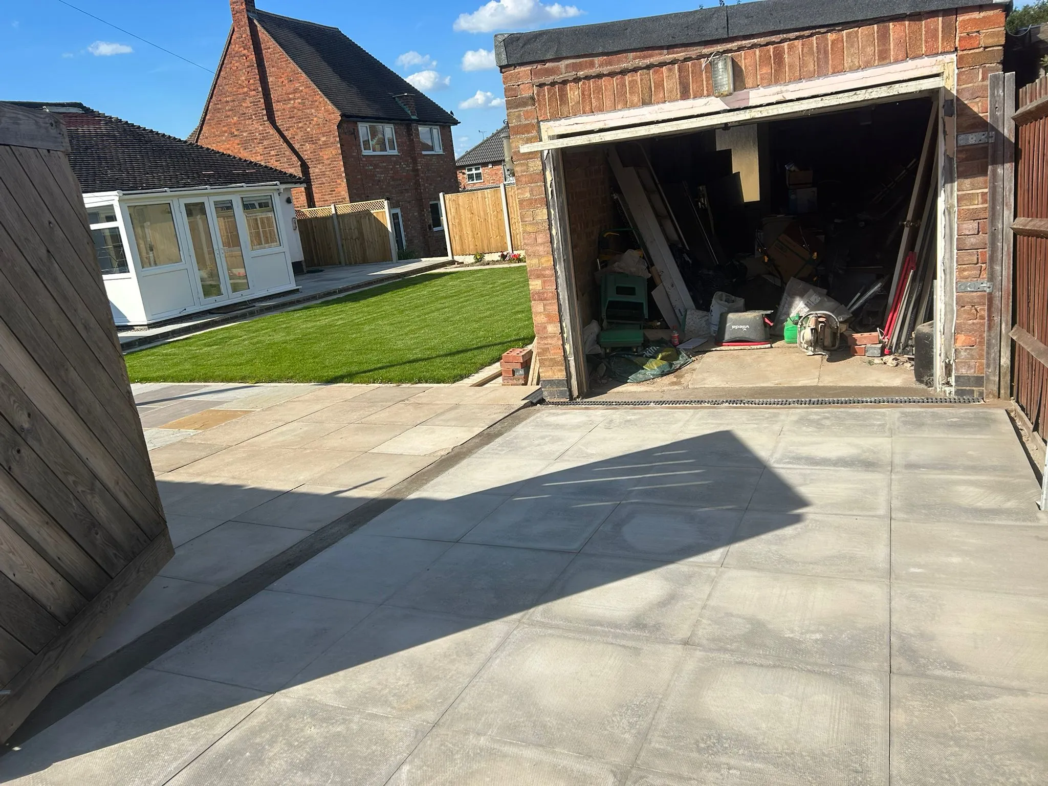 New grey patio slabs with drainage, a freshly laid green lawn, and new timber fencing in a recently landscaped garden.