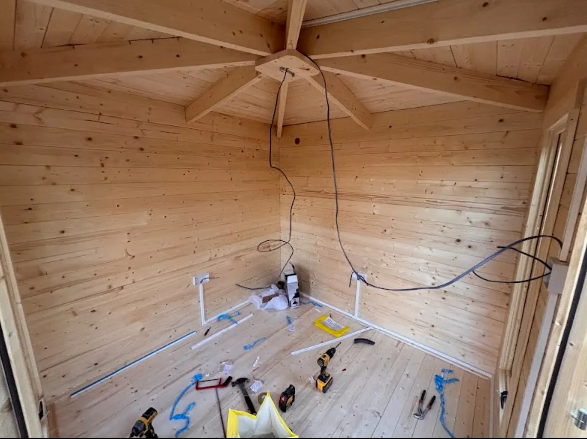 Electrical installation in progress inside a wooden garden room showing socket wiring and trunking