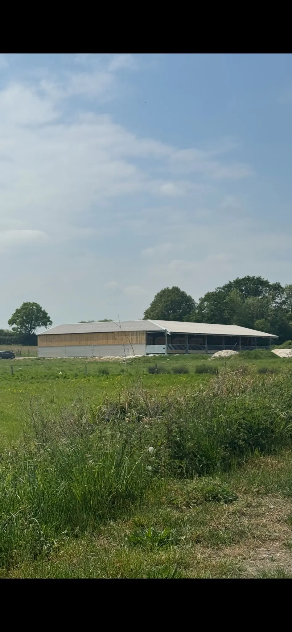 A newly built agricultural farm shed with timber cladding and a concrete lower wall situated in a rural field