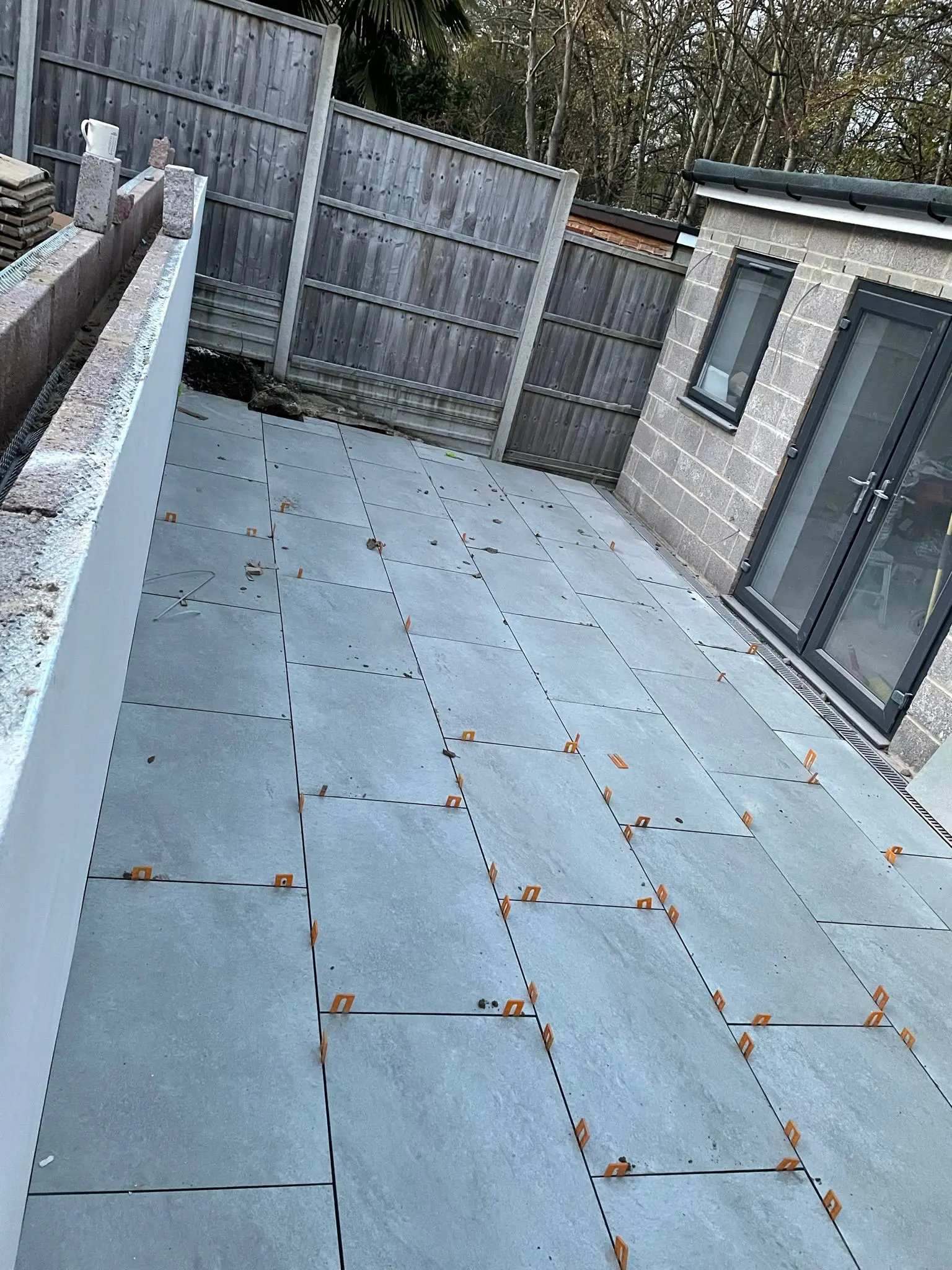 Grey porcelain patio installation in progress with orange levelling spacers in a residential garden