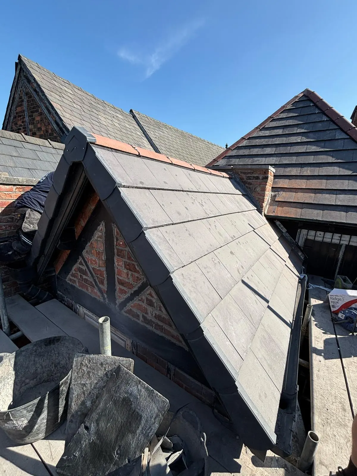 A roofer installing new grey roof tiles and a dry verge system on a pitched roof extension.