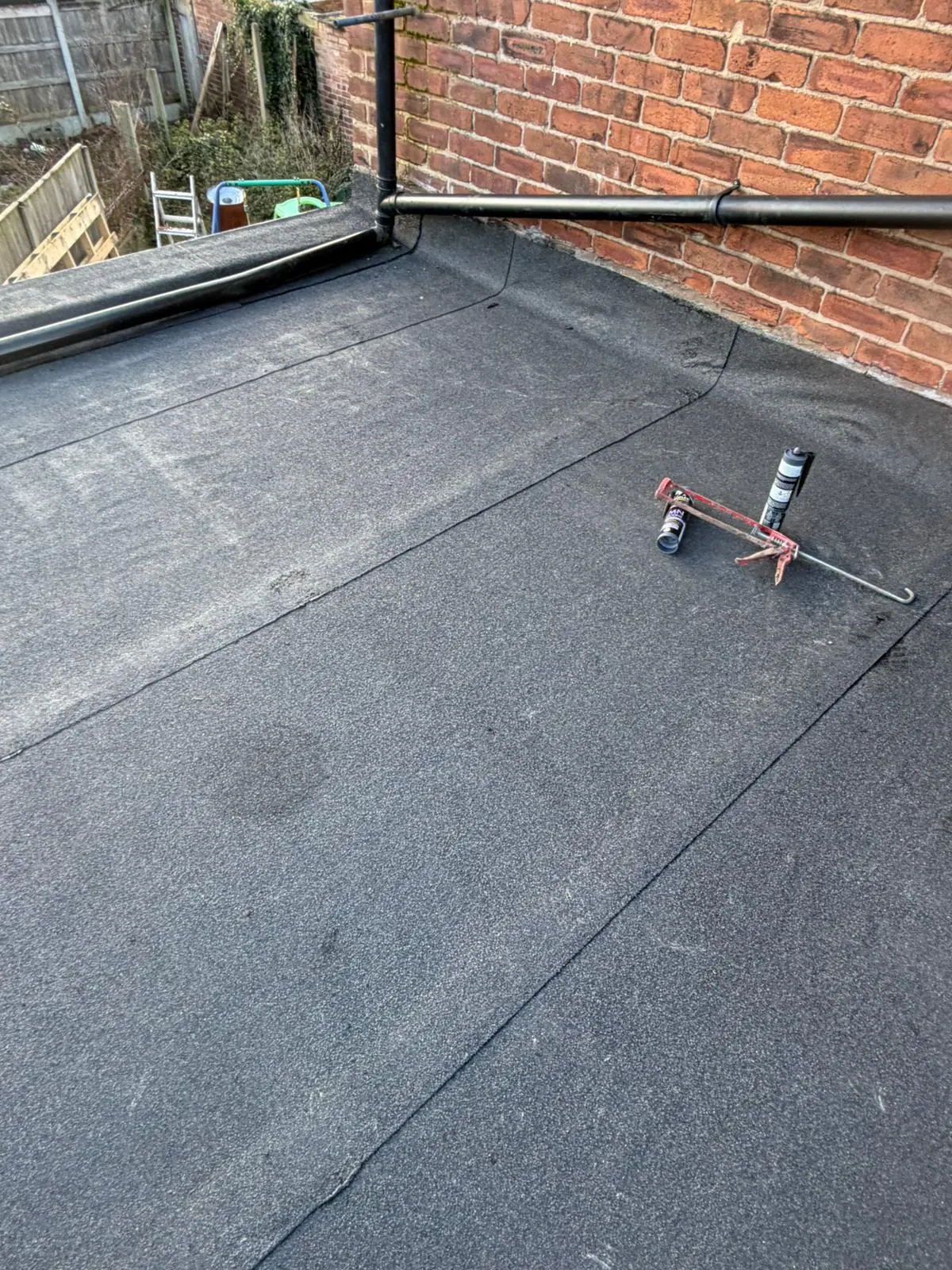 Completed flat felt roof installation showing secure seams and roofing sealant tools next to a brick wall.