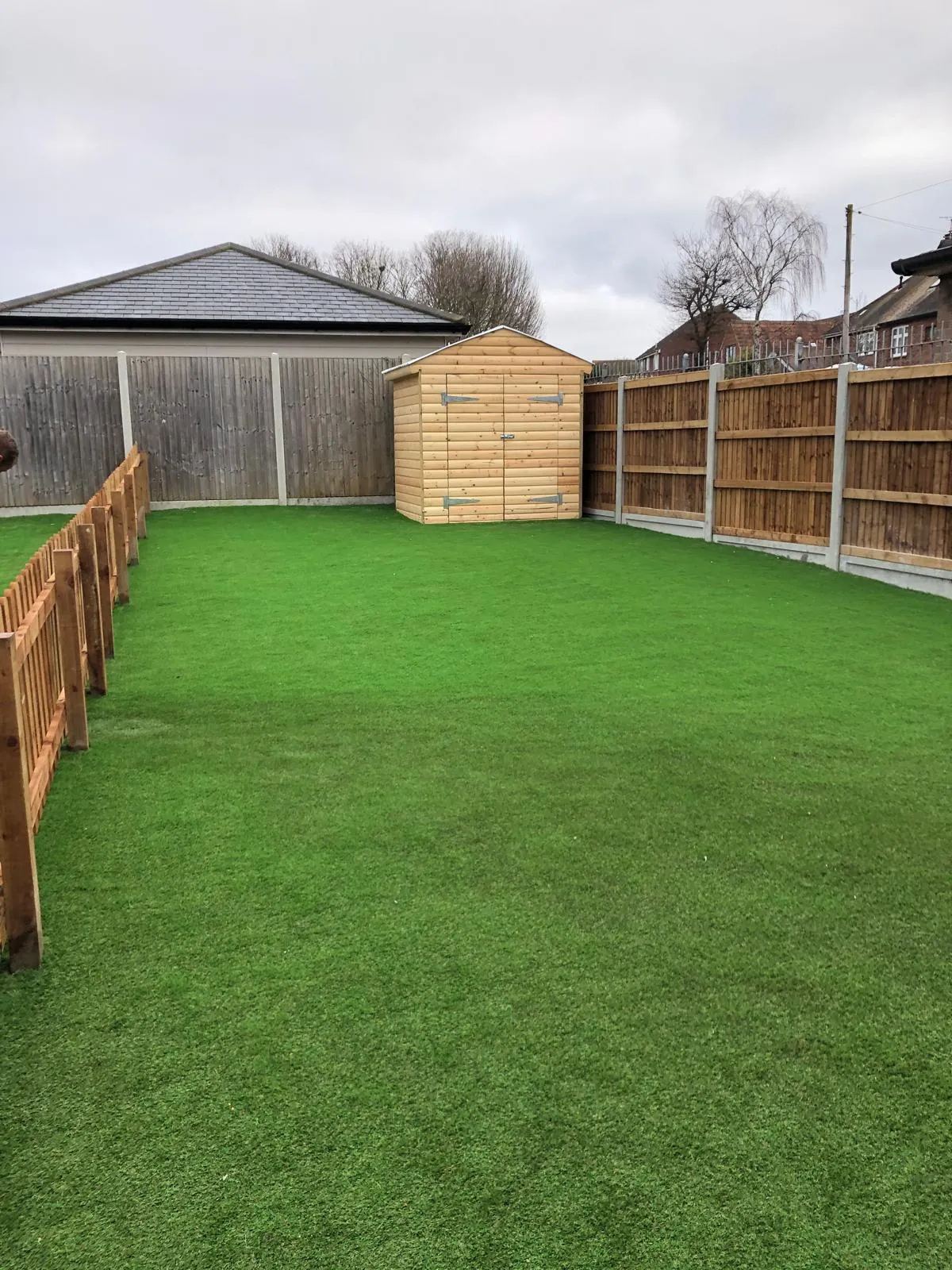 A modern garden with artificial lawn, new wooden shed, and two types of timber fencing.