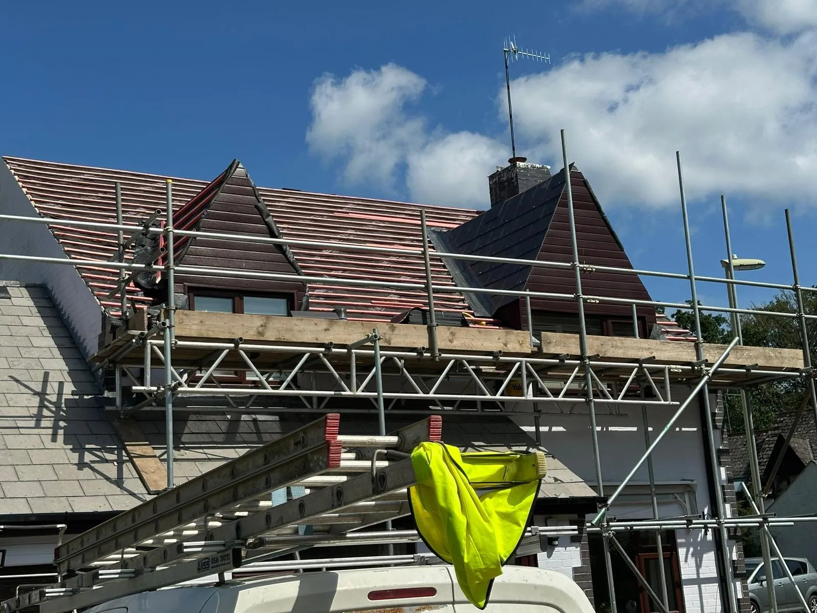 A house undergoing roof replacement with scaffolding, showing new roof battens and underlay before new tiles are installed.