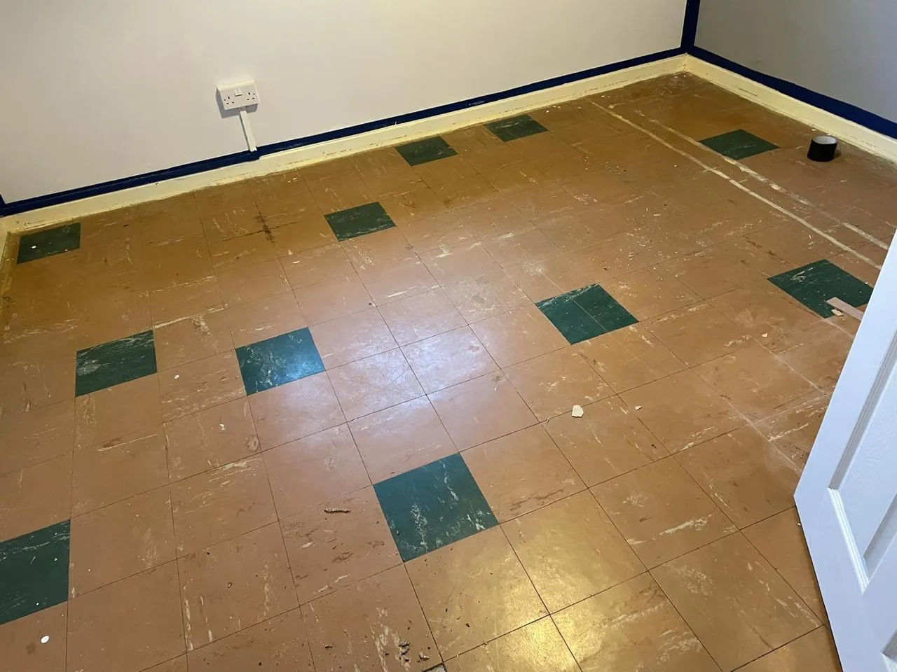 A room in a home featuring old, worn floor tiles, some brown/beige and some green, typical of asbestos-containing floor tiles, awaiting removal.