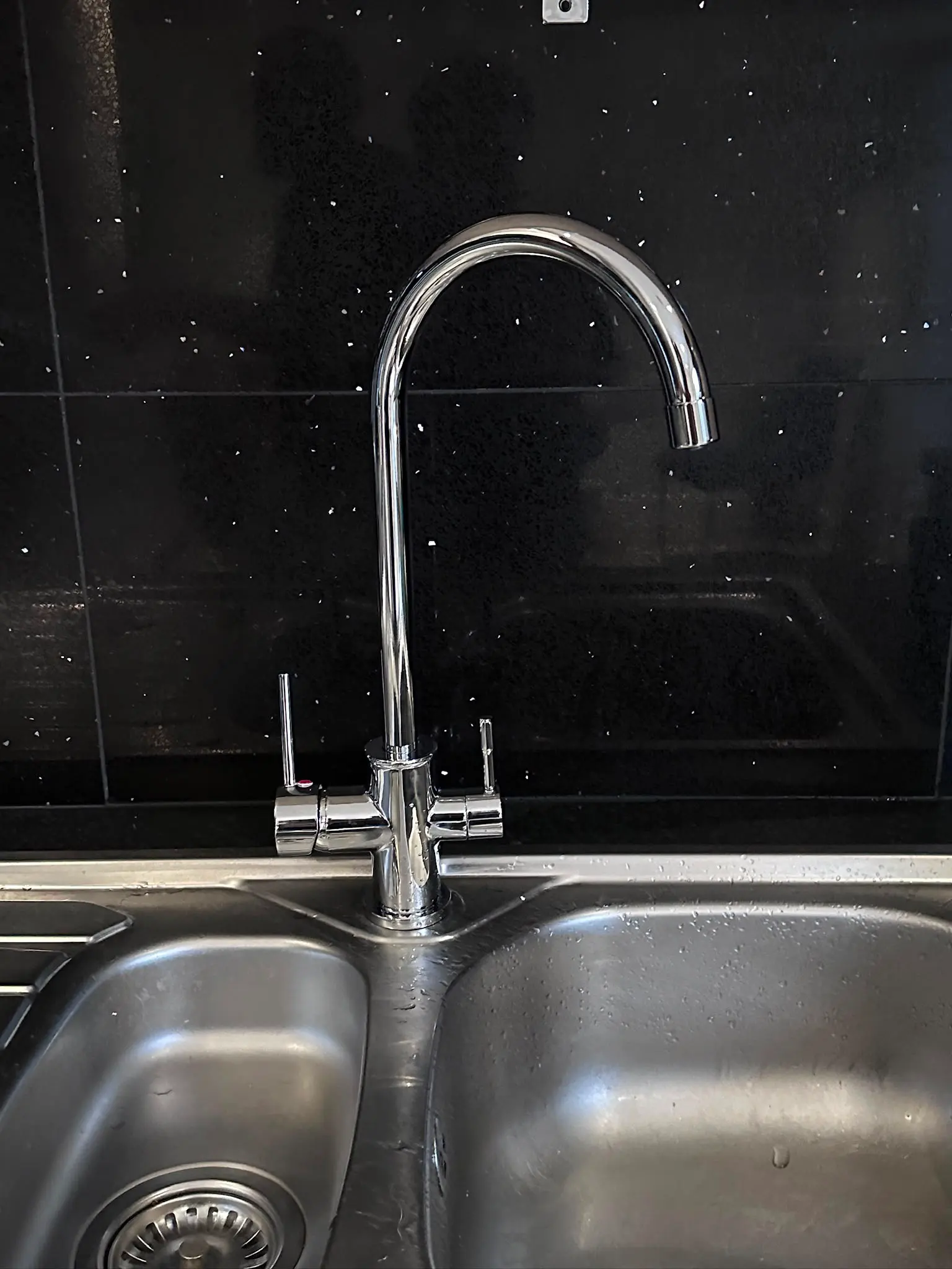 Newly installed modern chrome kitchen mixer tap on a stainless steel sink
