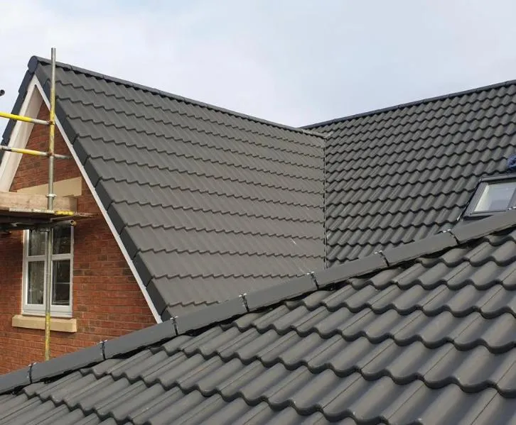 New dark grey tile roof installation with a Velux window and scaffolding on a residential building.
