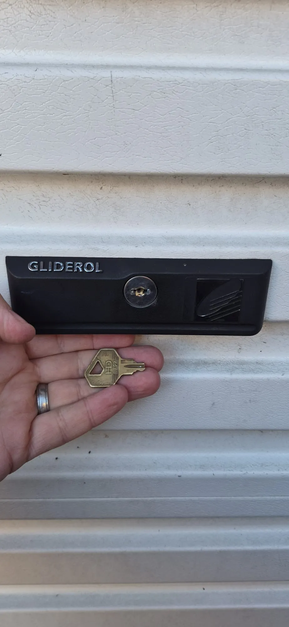 A replacement key being held up to a Gliderol garage door lock by a locksmith.