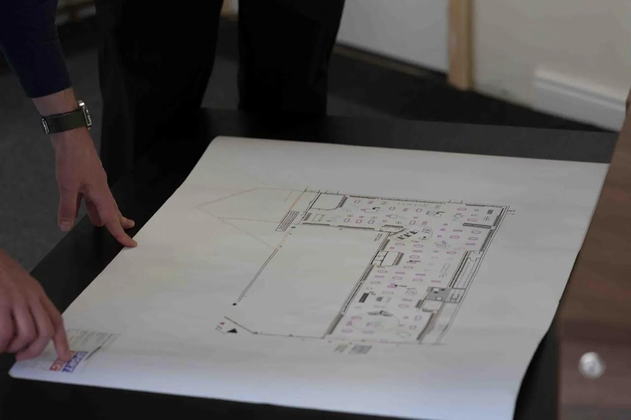 Hands pointing at and reviewing a complex building floor plan for an asbestos survey or removal project.