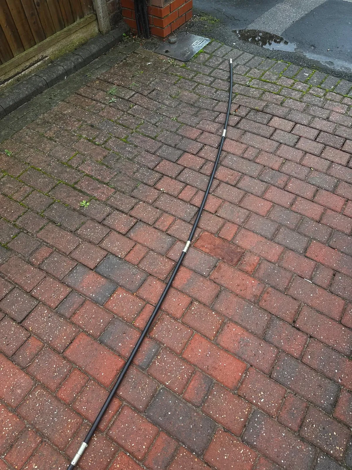 A professional drain rod on a patterned brick driveway, used for unblocking drains.