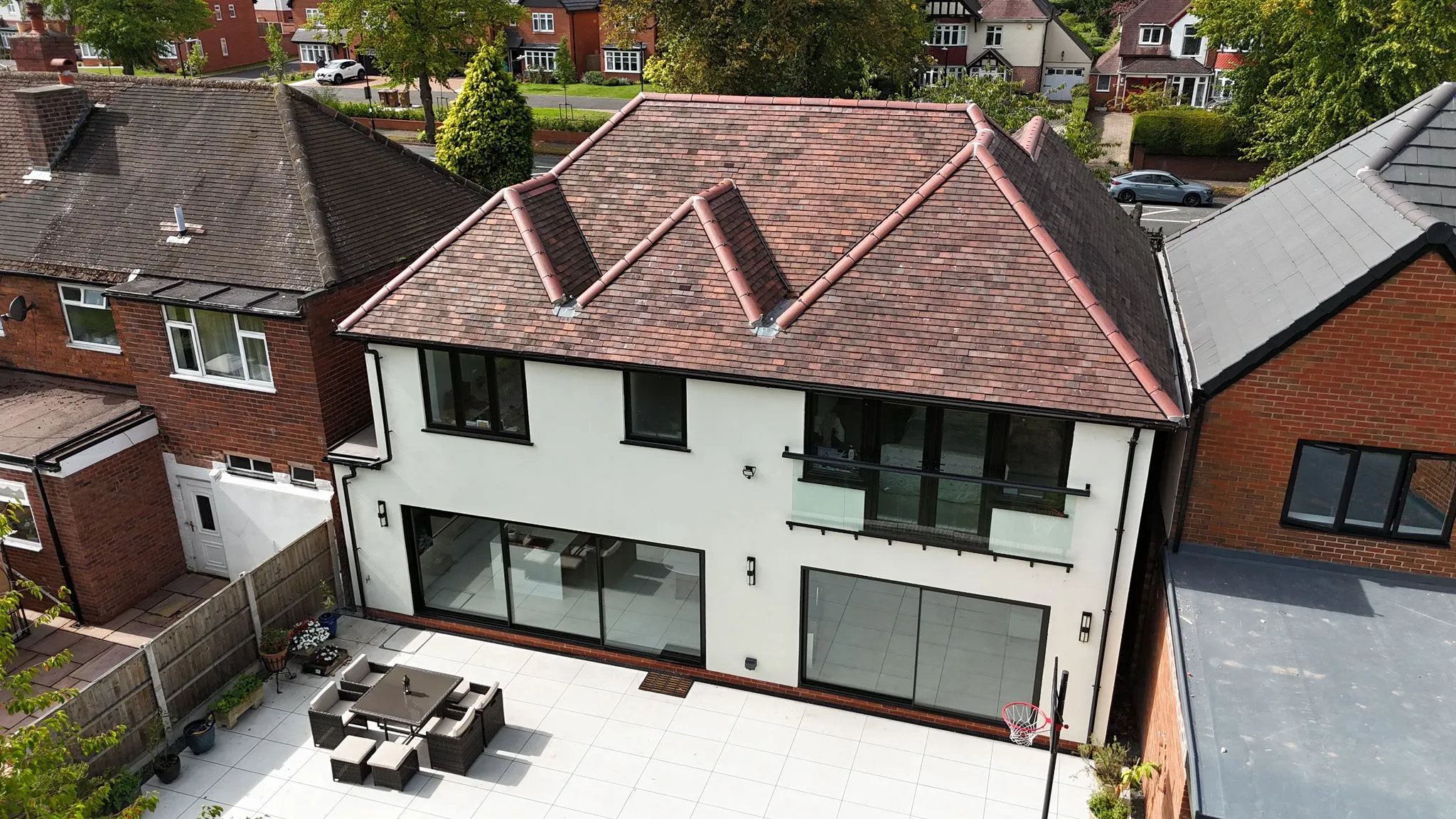 Aerial view of a modern, newly built two-storey home extension with large glass doors, a balcony, and a patio.