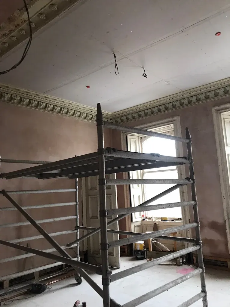 Interior wall and ceiling plastering work in progress with scaffolding in a traditional room.