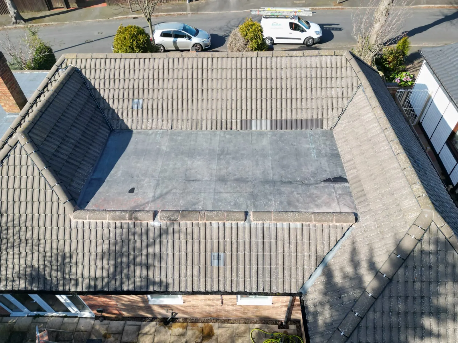 Aerial view of a residential house roof, showing a combination of pitched tiled roofing and a flat roof system.