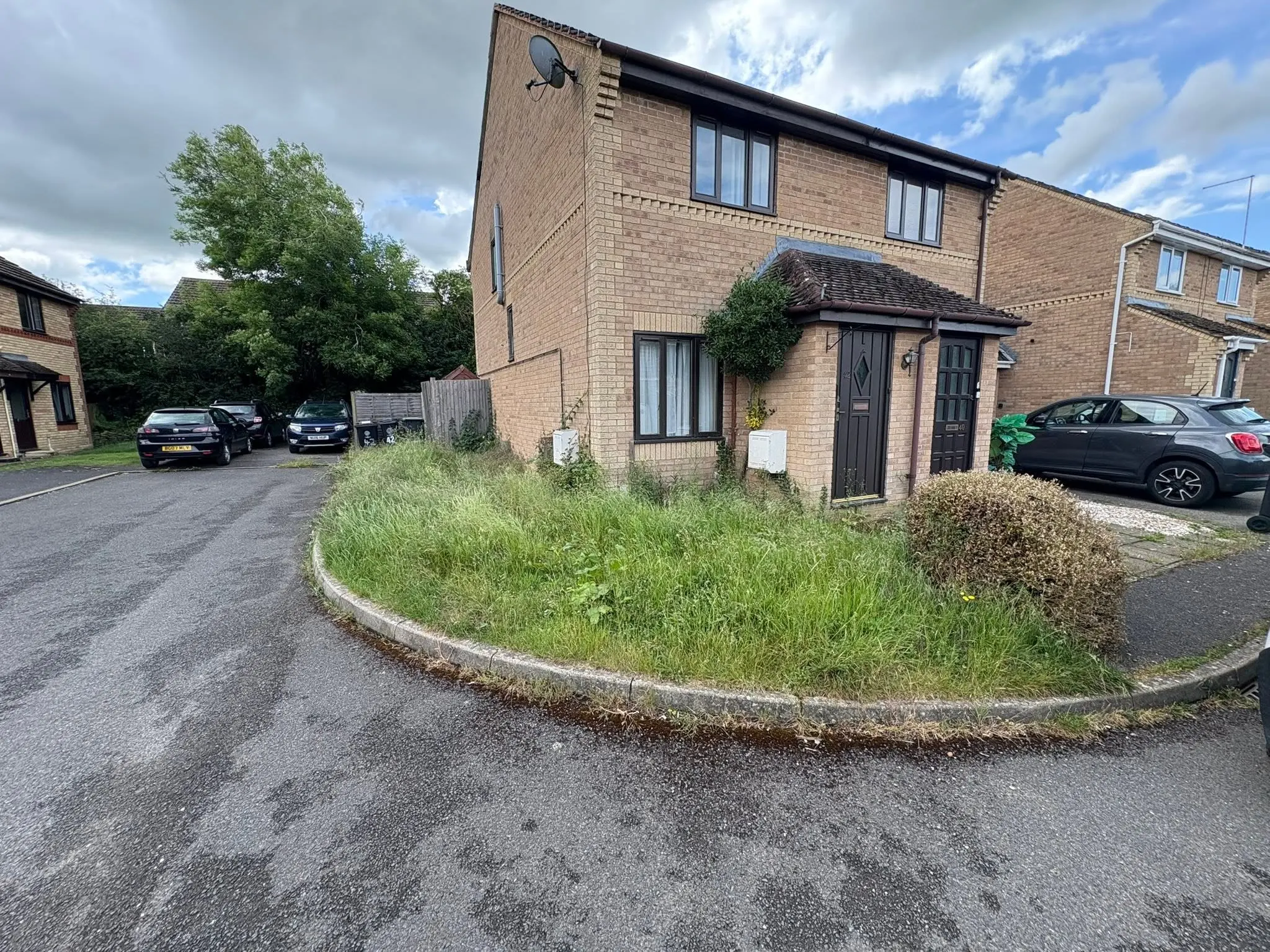 Overgrown front garden with long grass outside a brick house, needing garden clearance or maintenance