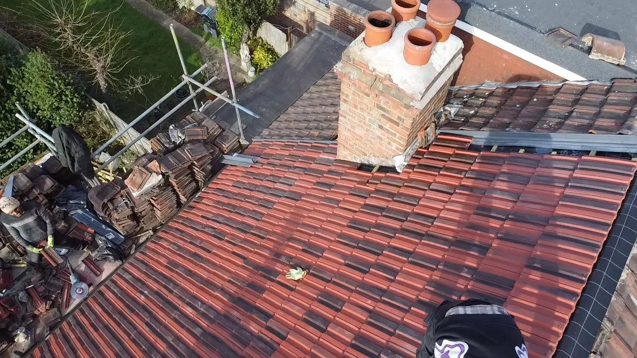 Roofer installing or replacing tiles on a pitched roof with scaffolding and a brick chimney