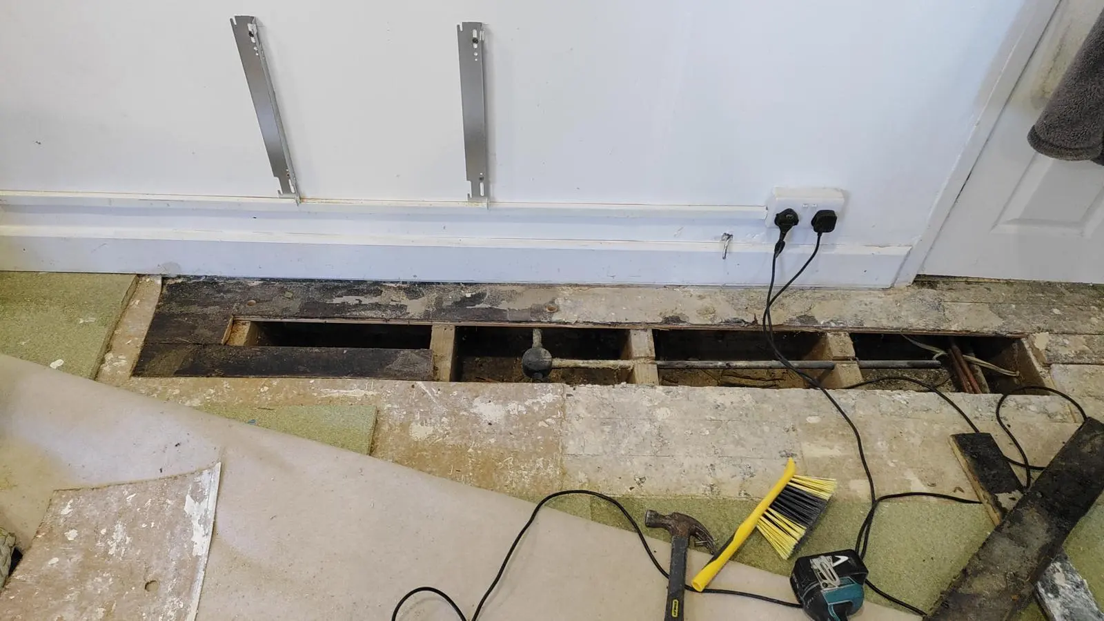 Floorboards removed to show pipework and joists for leak detection and repair by a plumber.
