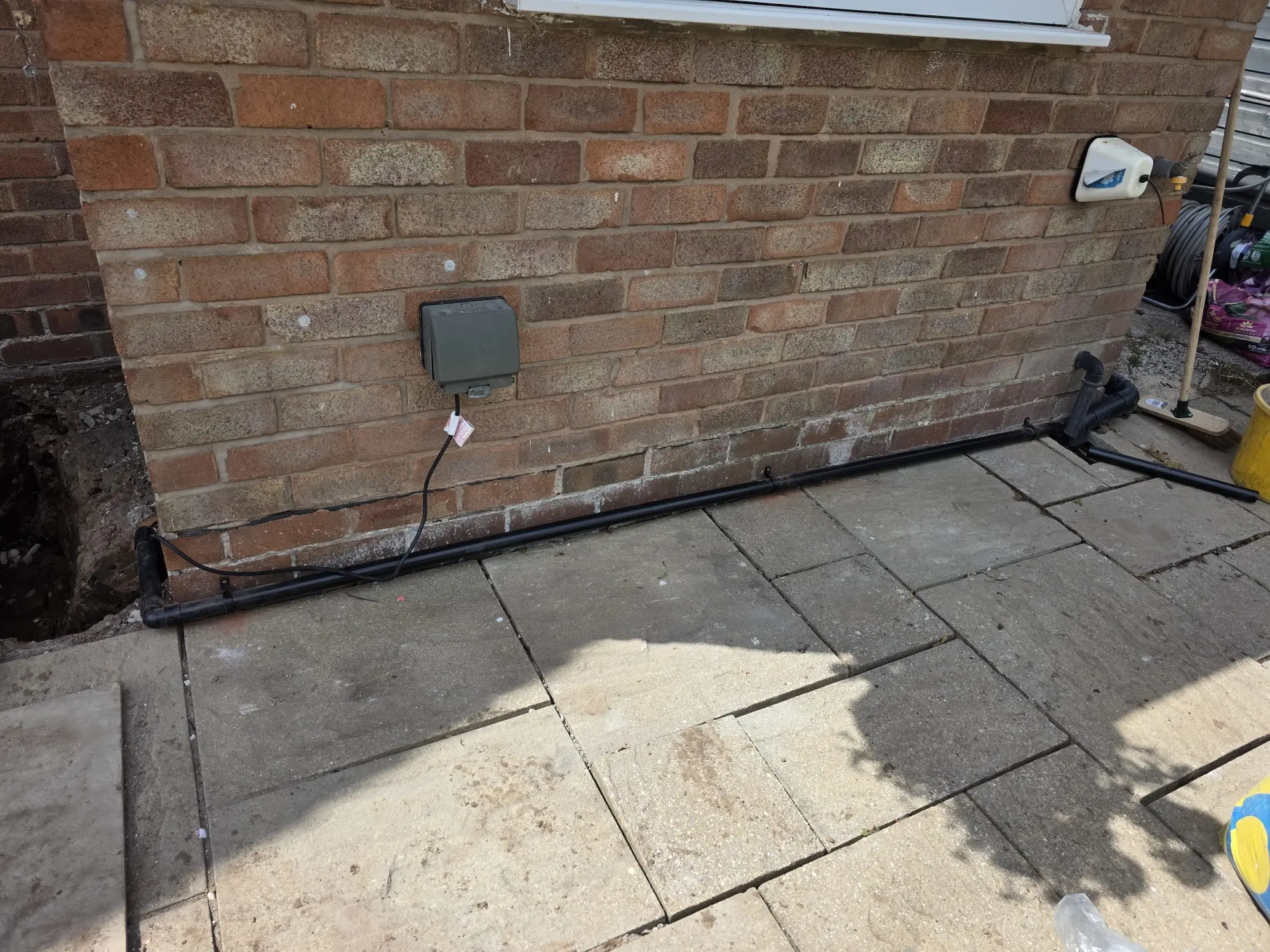 Black exterior drainage pipe installed along a brick wall for a domestic drain repair in Cheshire.