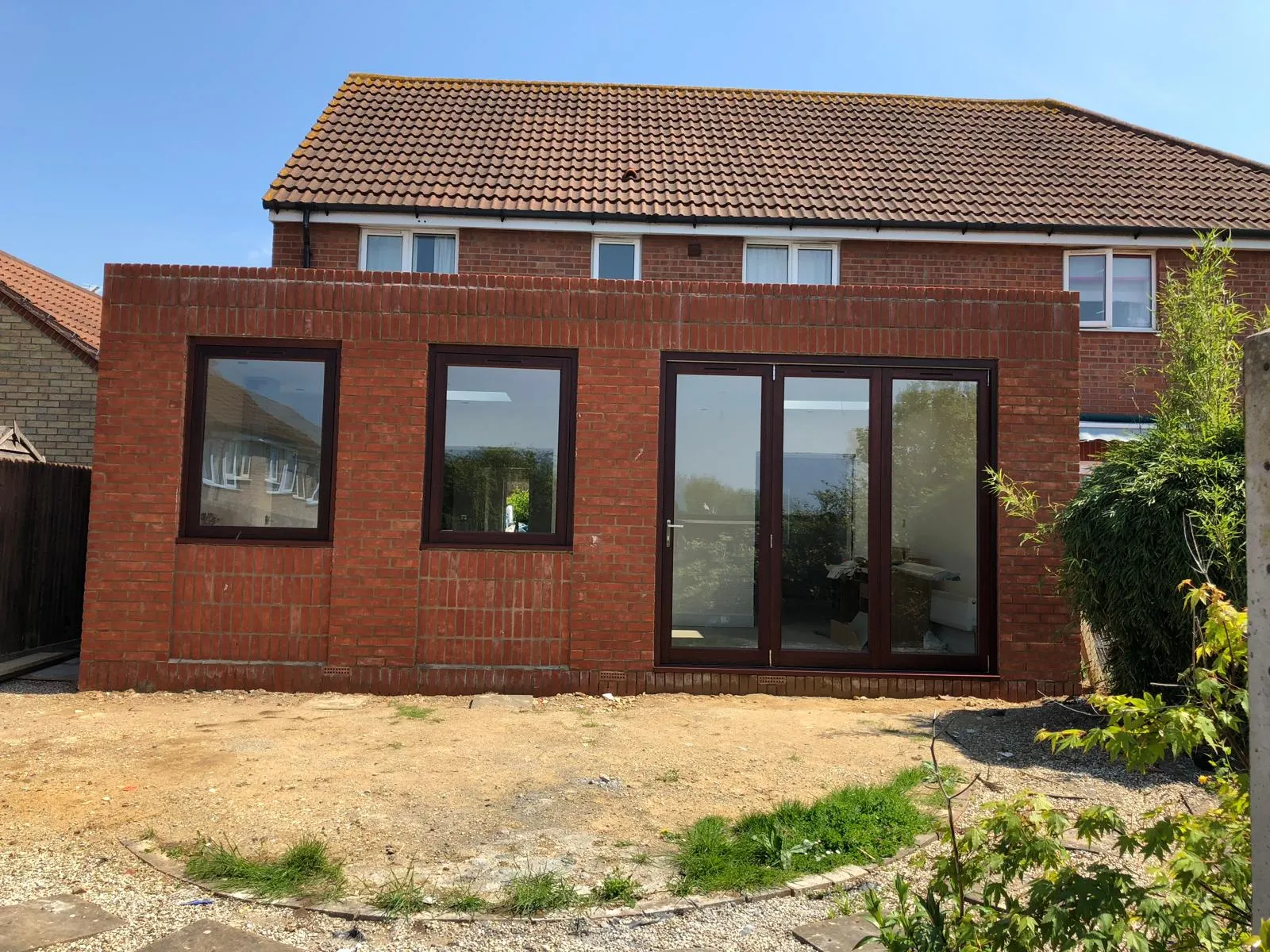 A completed red brick house extension with bifold doors and two windows, ready for internal fit-out and landscaping