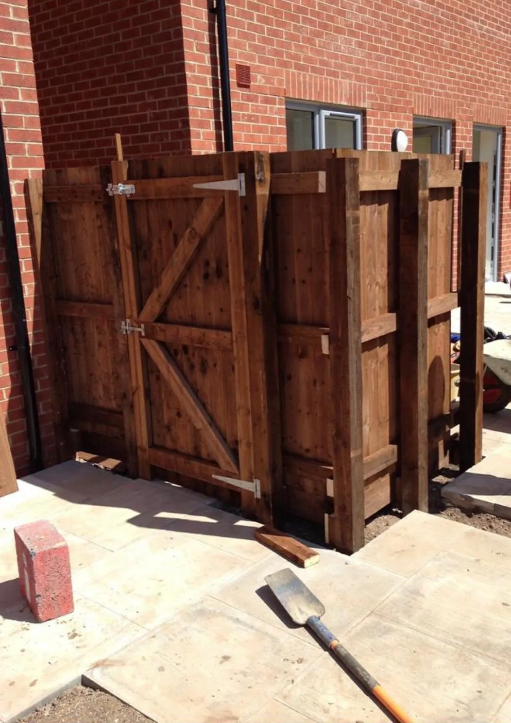 Bespoke wooden gate or privacy screen being installed on a newly paved patio during landscaping work.
