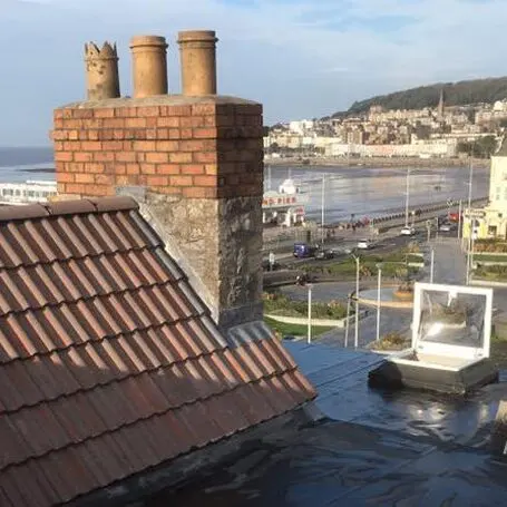 Pitched tiled roof and brick chimney stack overlooking a coastal town