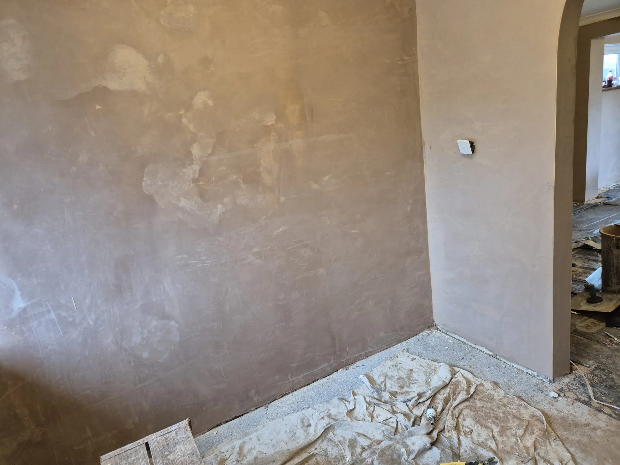 Newly plastered interior walls in a domestic renovation project, with a visible electrical socket and dust sheet.