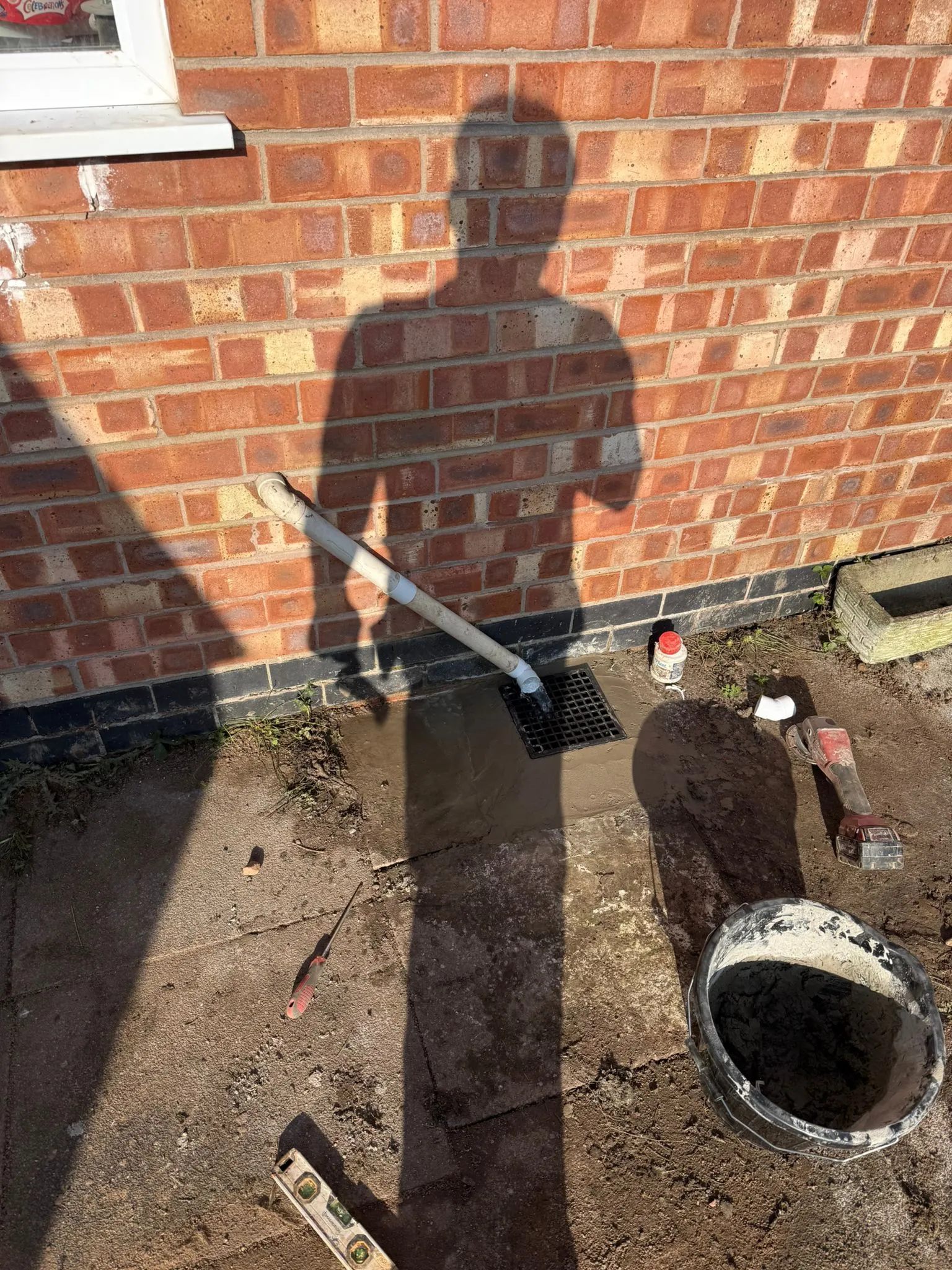 A newly installed external gully drain and waste pipe against a brick wall