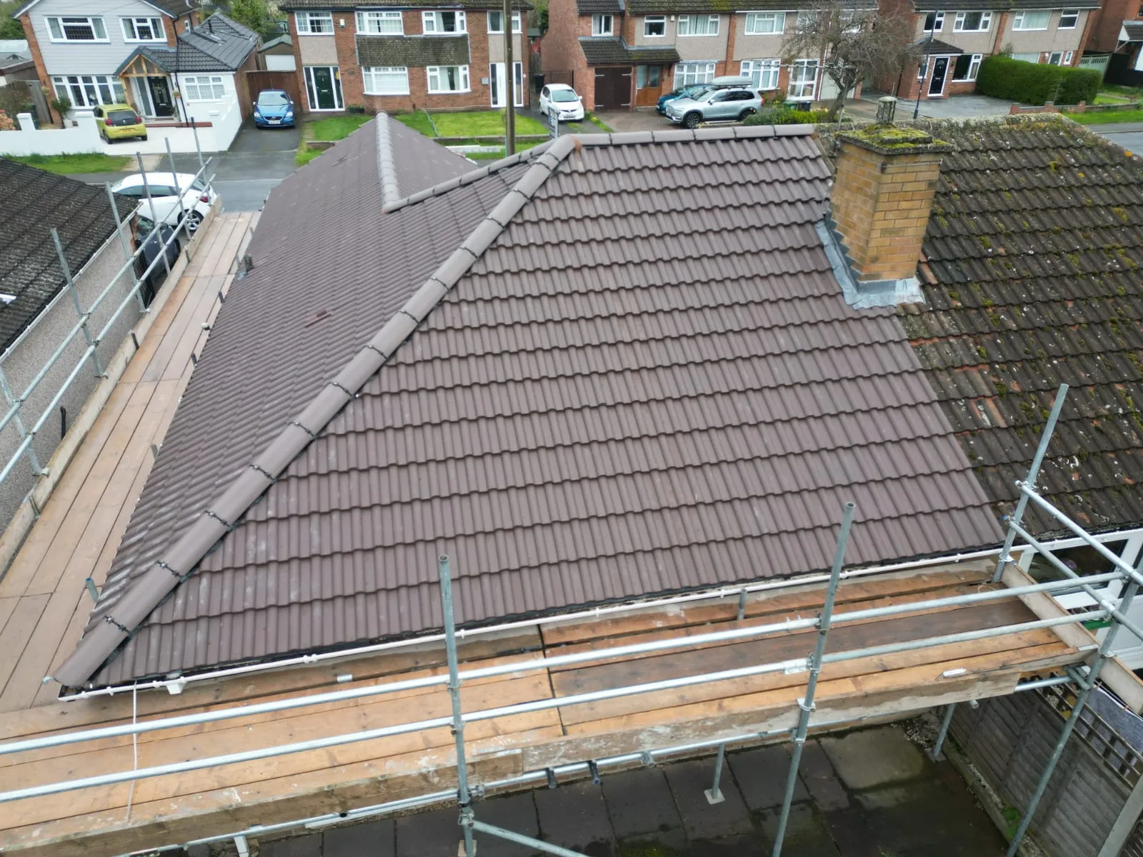 New brown tiled pitched roof alongside old mossy roof, with scaffolding around the property, indicating a re-roofing project.