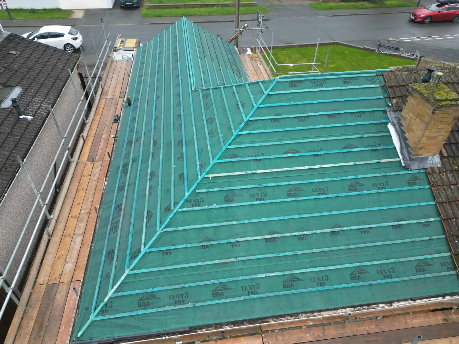 New pitched roof under construction with green membrane and wooden battens, scaffolding around the house.