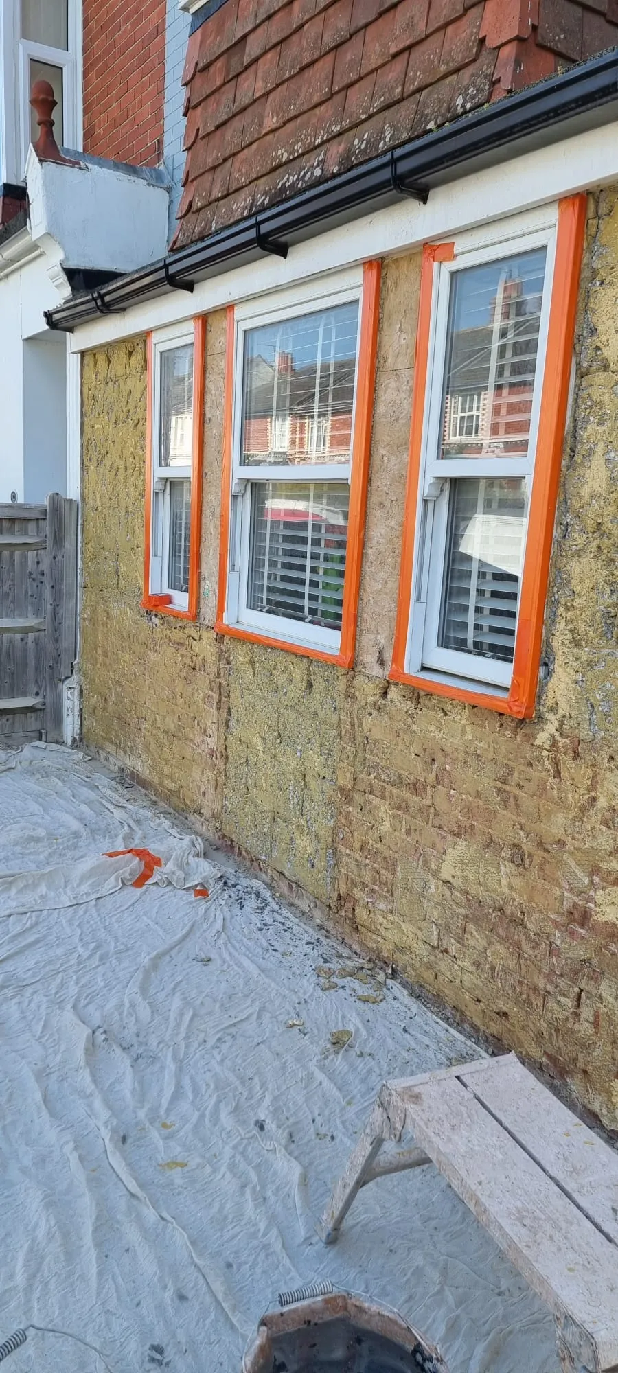 Preparation of an exterior wall for rendering, showing masked windows and exposed brickwork.