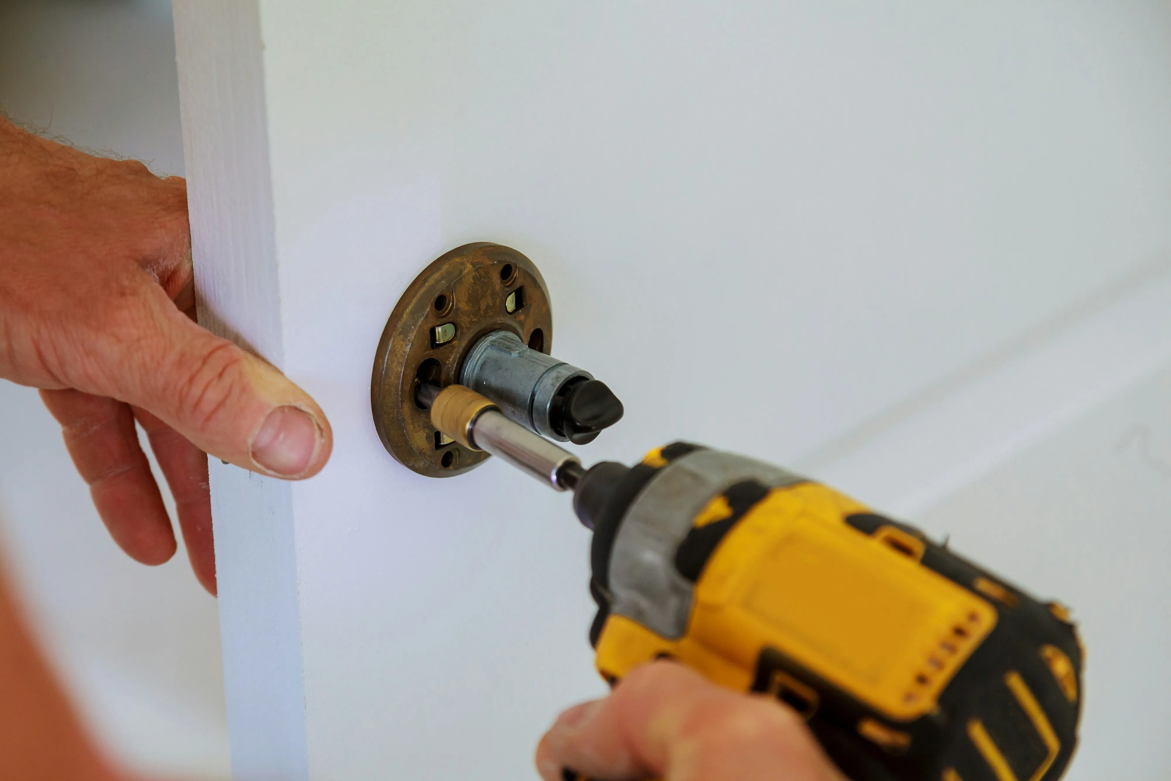 Hands using a power drill to install or repair a door lock mechanism on a white door.
