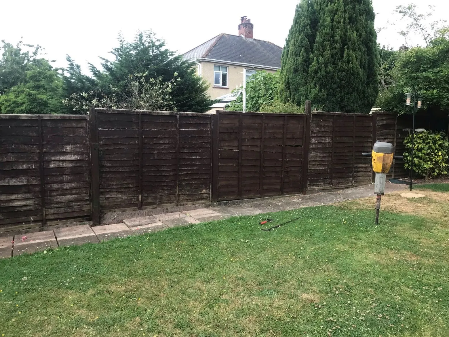 Weathered timber fence line with breaker tool prepared for fence post repairs and replacement in a garden