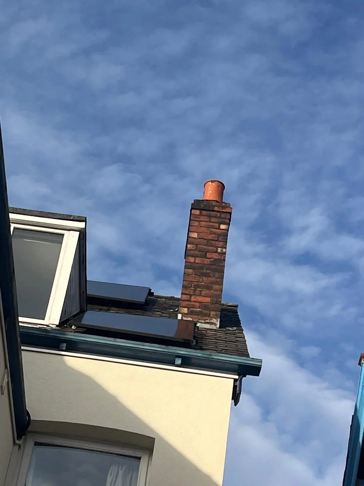 A brick chimney stack and solar panels on a slate roof