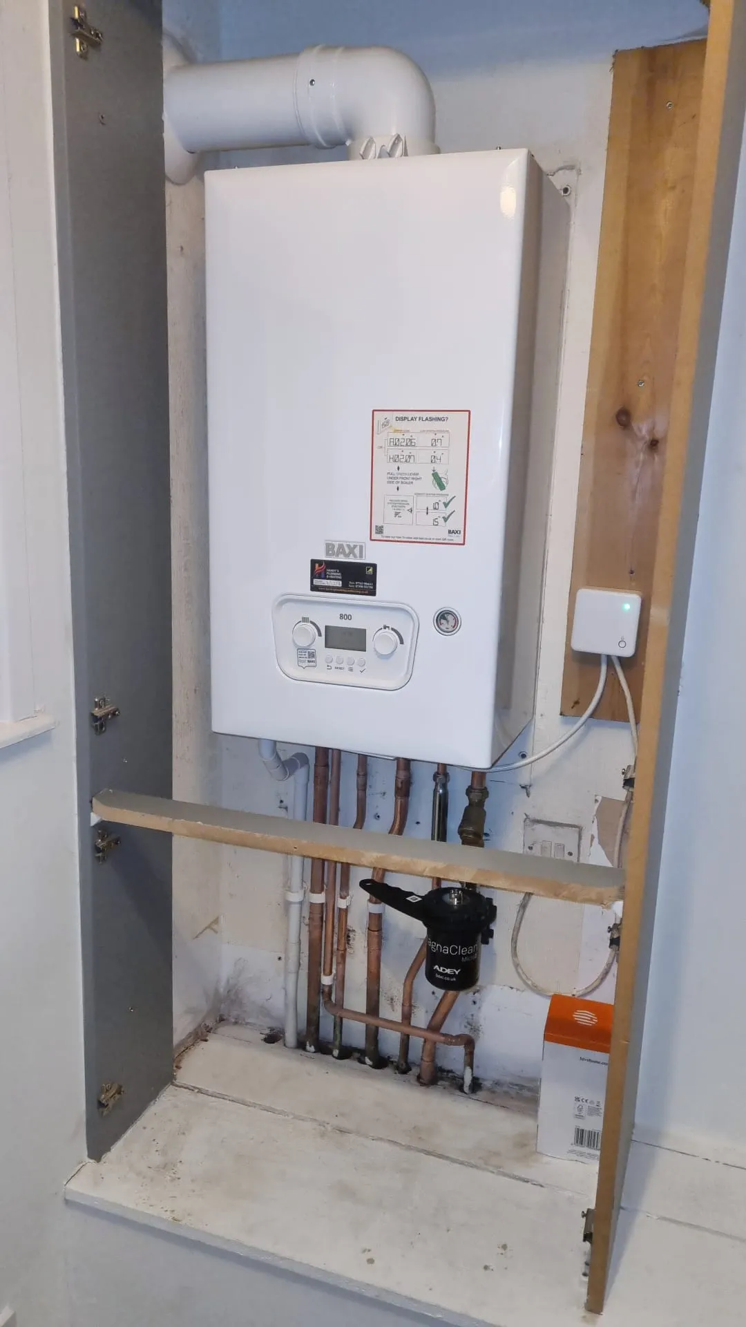 A white Baxi boiler mounted on a wall with copper pipes and a magnetic filter, representing boiler installation and heating services.