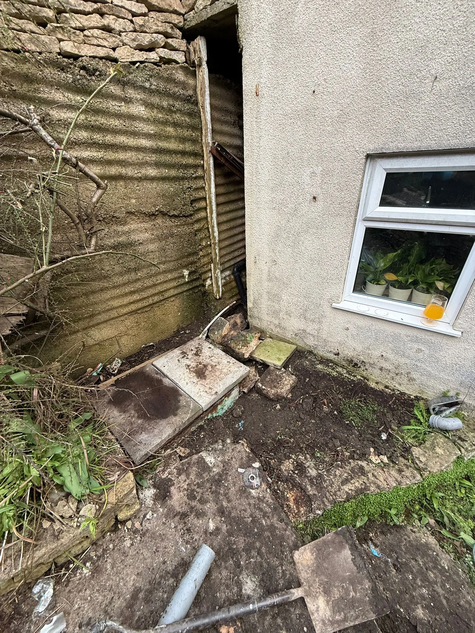 A drainage repair site at a house showing a shovel and access to underground pipes.