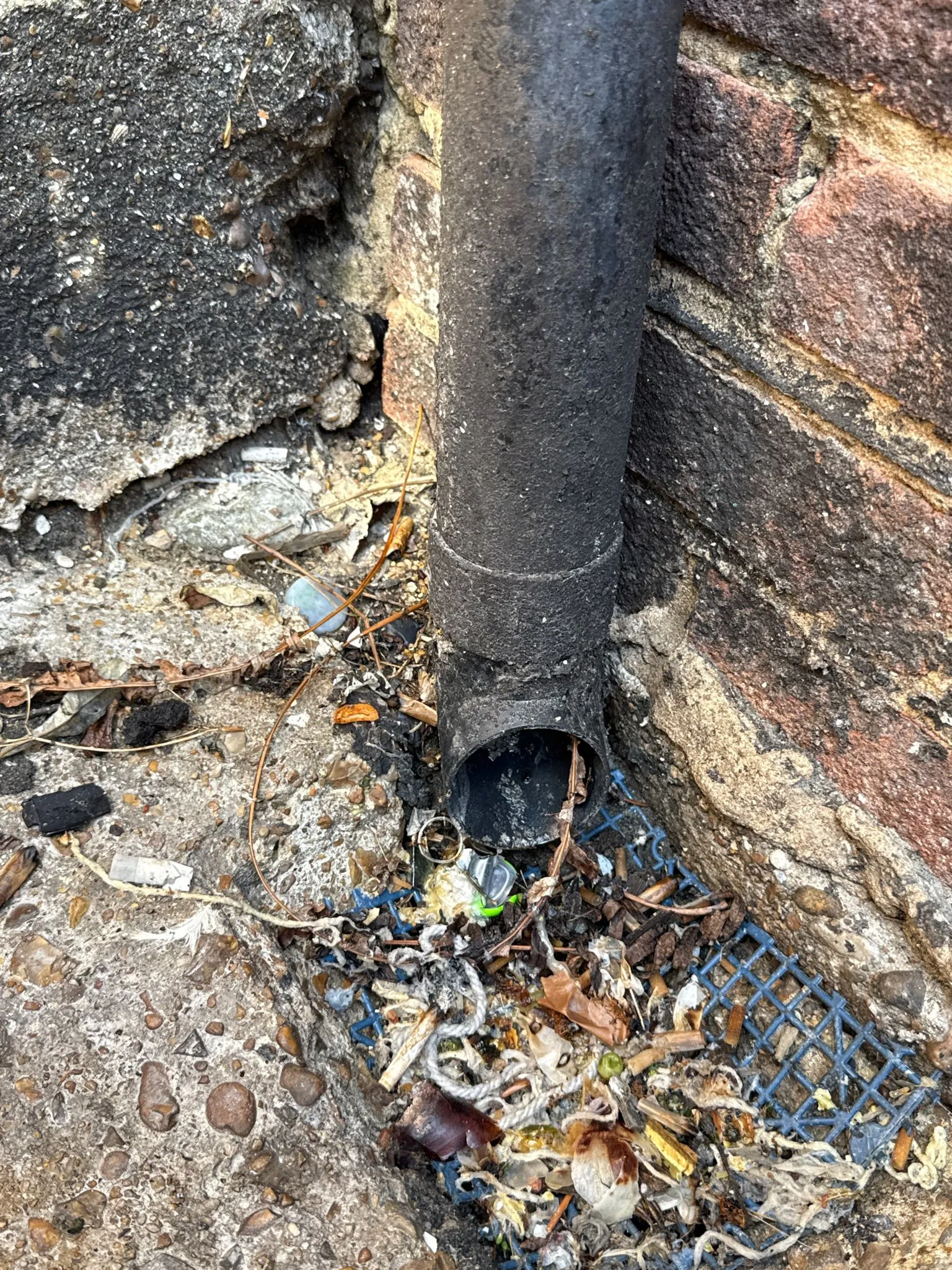 A picture of a blocked and dirty drain pipe outlet with debris