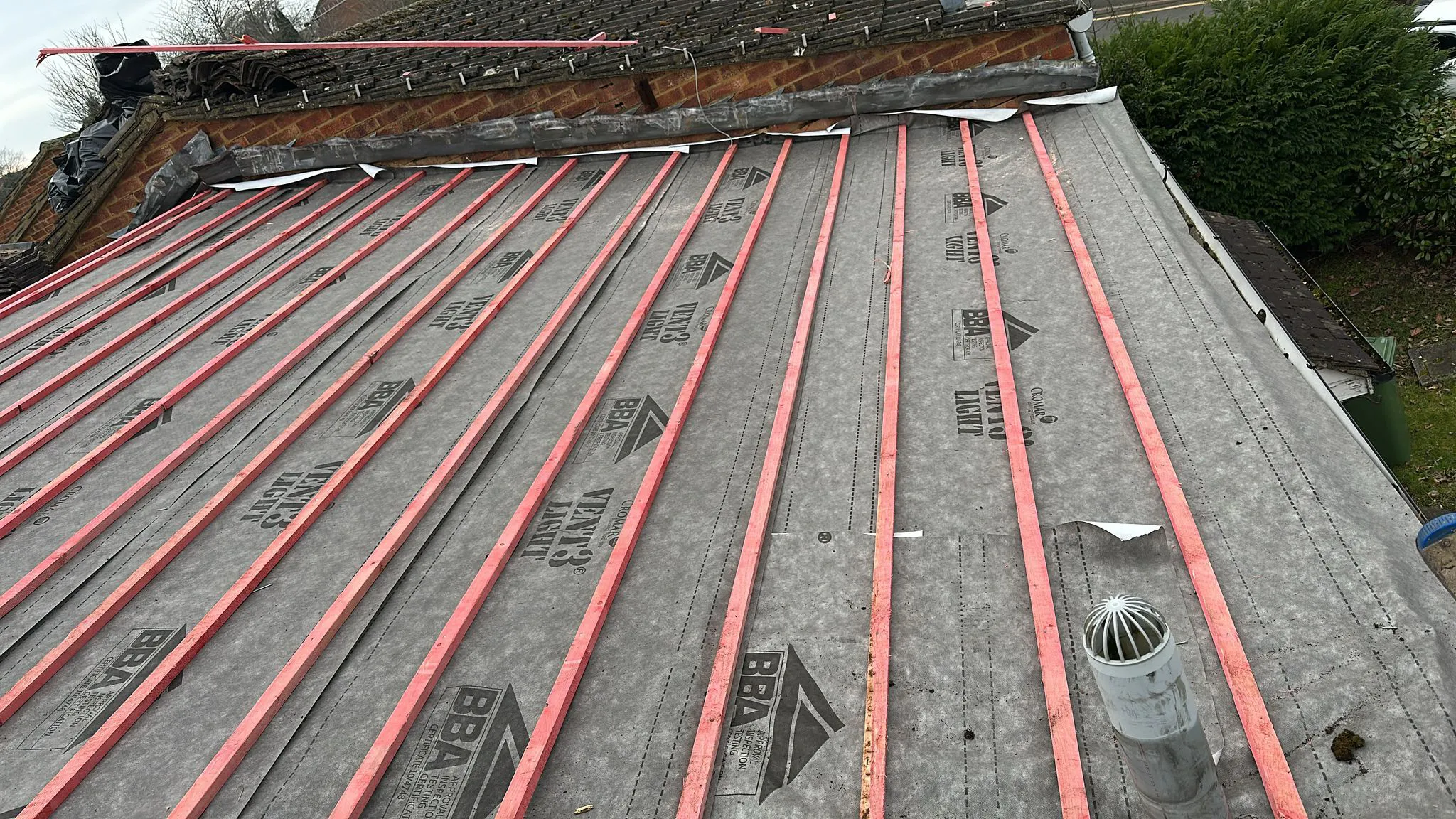 Vapour-permeable roof membrane and red timber battens fitted on a pitched roof ready for tiling