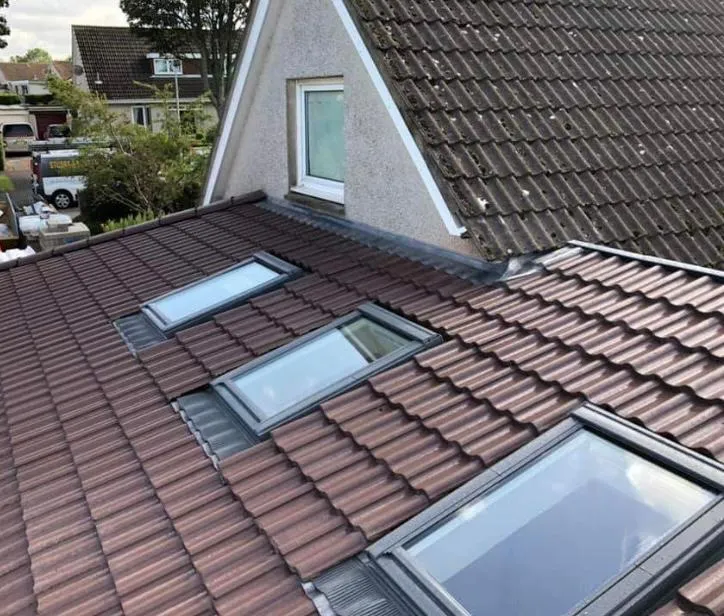 Newly installed brown roof tiles with three Velux windows, blending into an older, weathered tiled roof with a dormer.