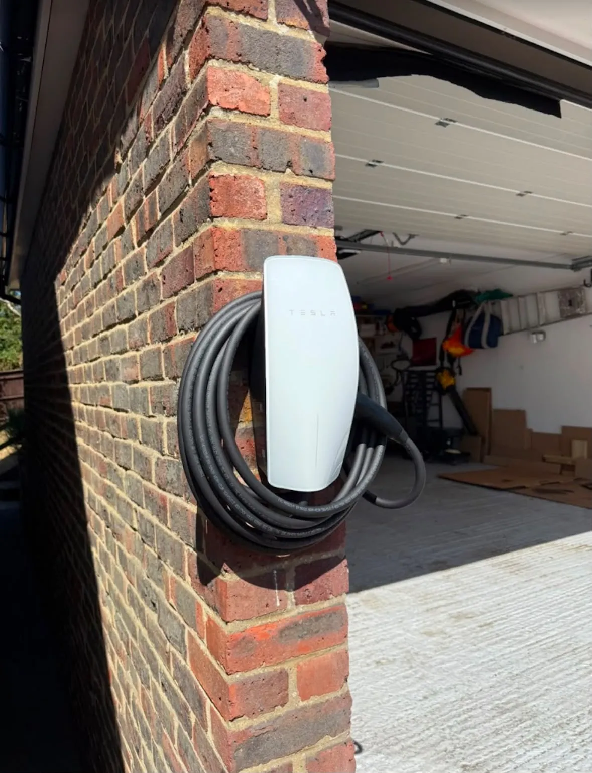 Domestic Tesla EV charger installation mounted on an exterior brick garage wall by Sussex Brown Sparks