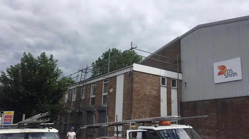 Commercial roofing contractors setting up scaffolding for roof repairs at an industrial building