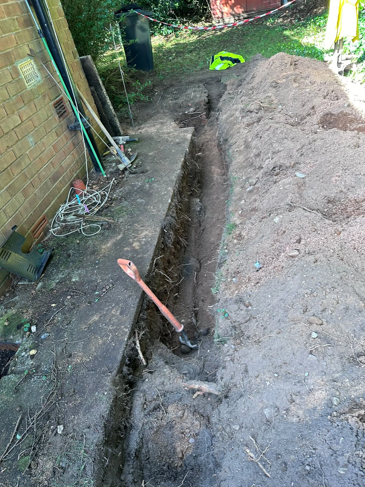 A long, deep trench excavated next to a brick house for professional drain repair services.