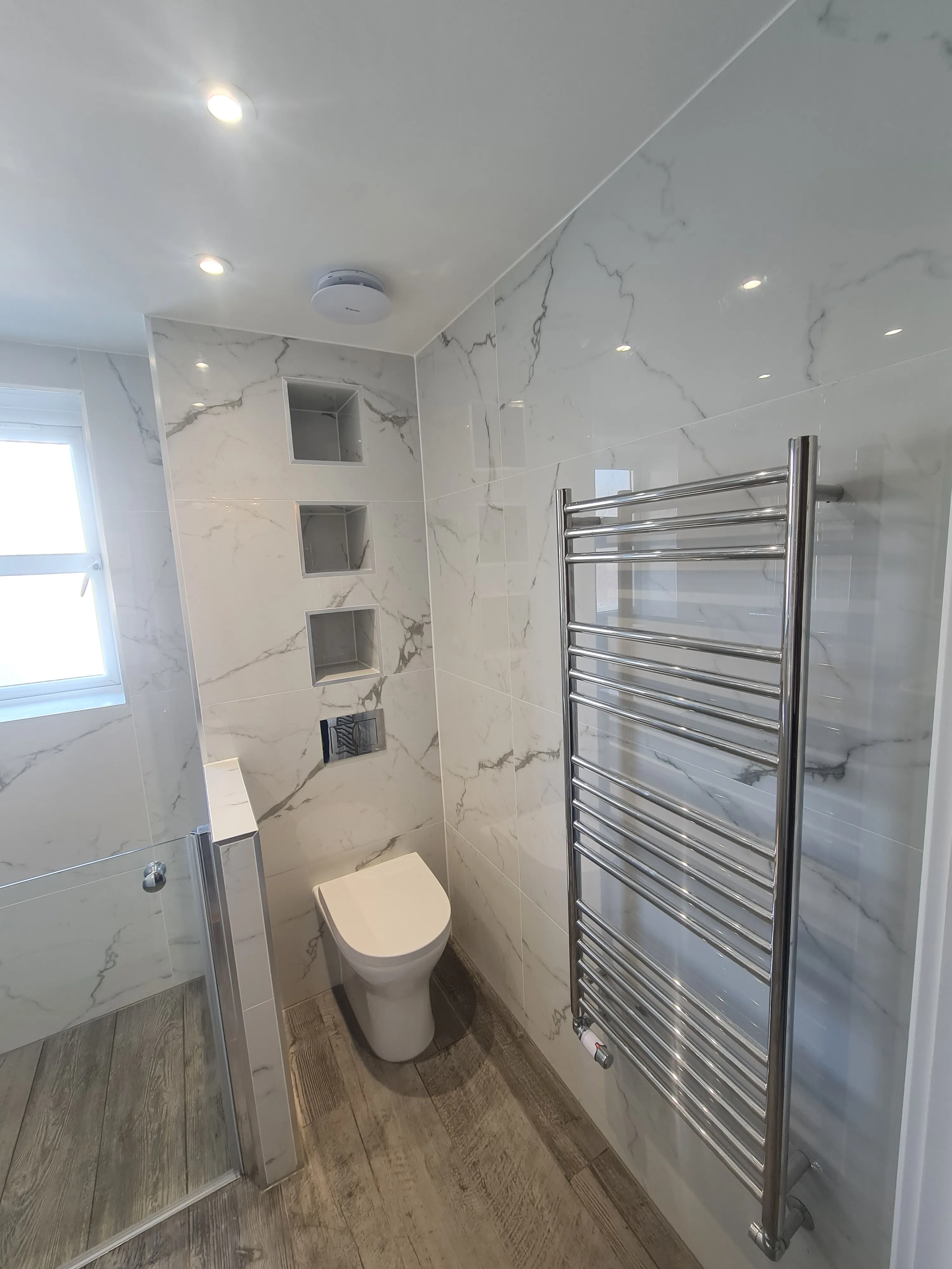 High-end bespoke bathroom installation in Plymouth featuring marble tiles and recessed shelving by Sands & Vossen.