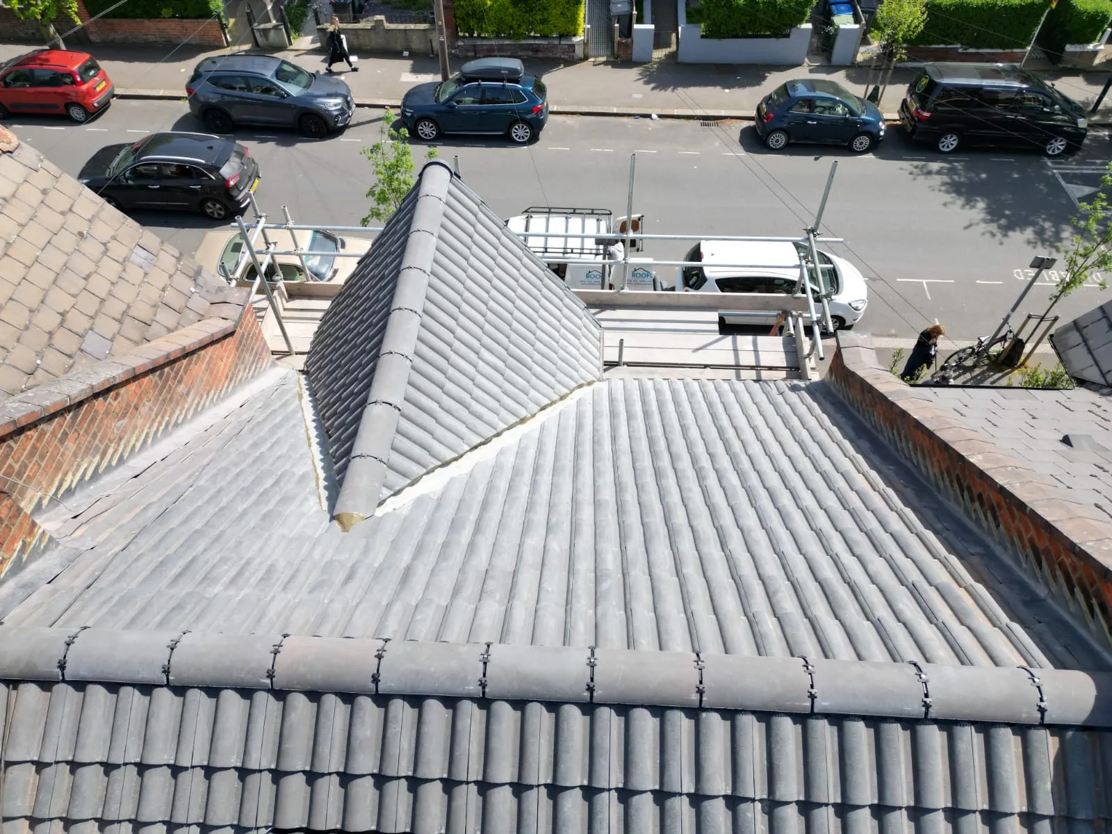 Overhead view of a tiled residential roof, showing new grey tiles, scaffolding, and Rooflex Roofing Solutions vans on the street.
