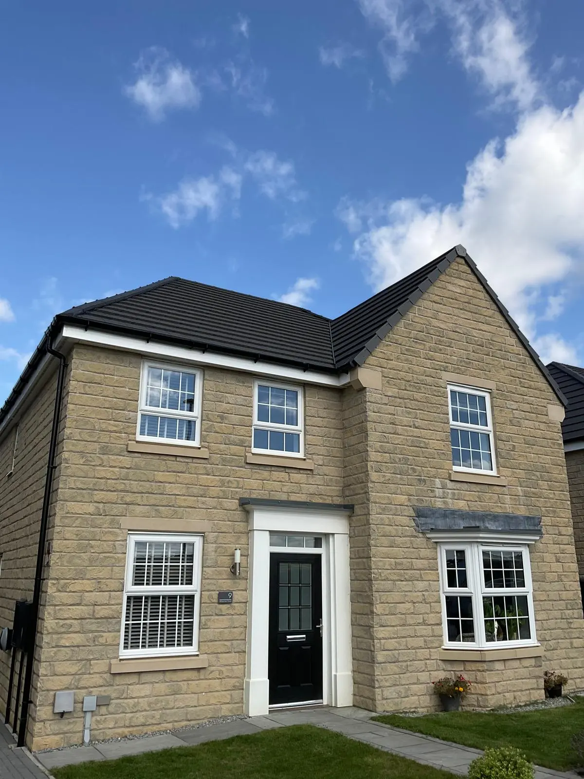 A modern stone house featuring a pristine, newly installed dark grey tiled pitched roof