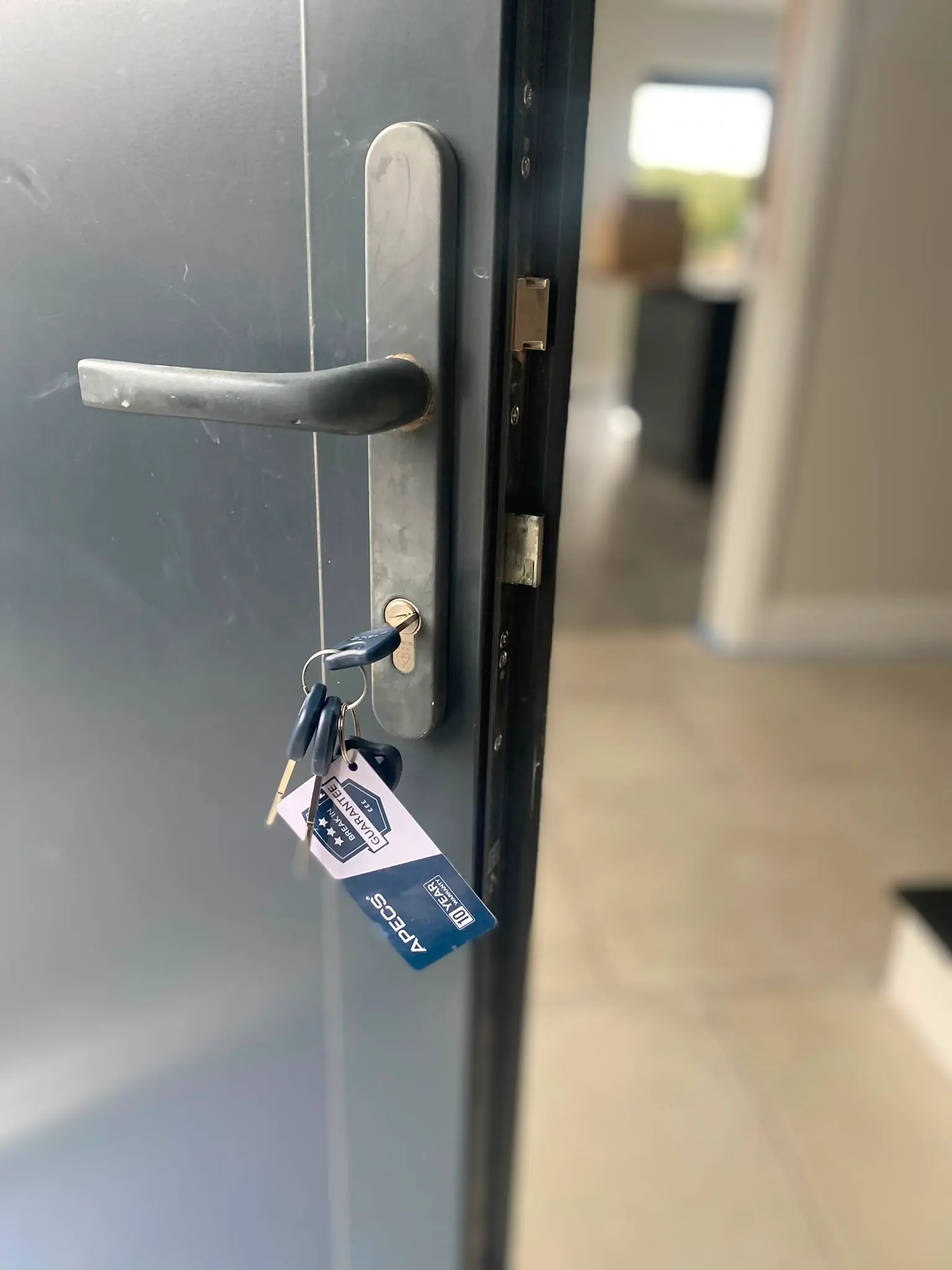 Newly installed APECS 3-star anti-snap euro cylinder lock with warranty tag on a residential door
