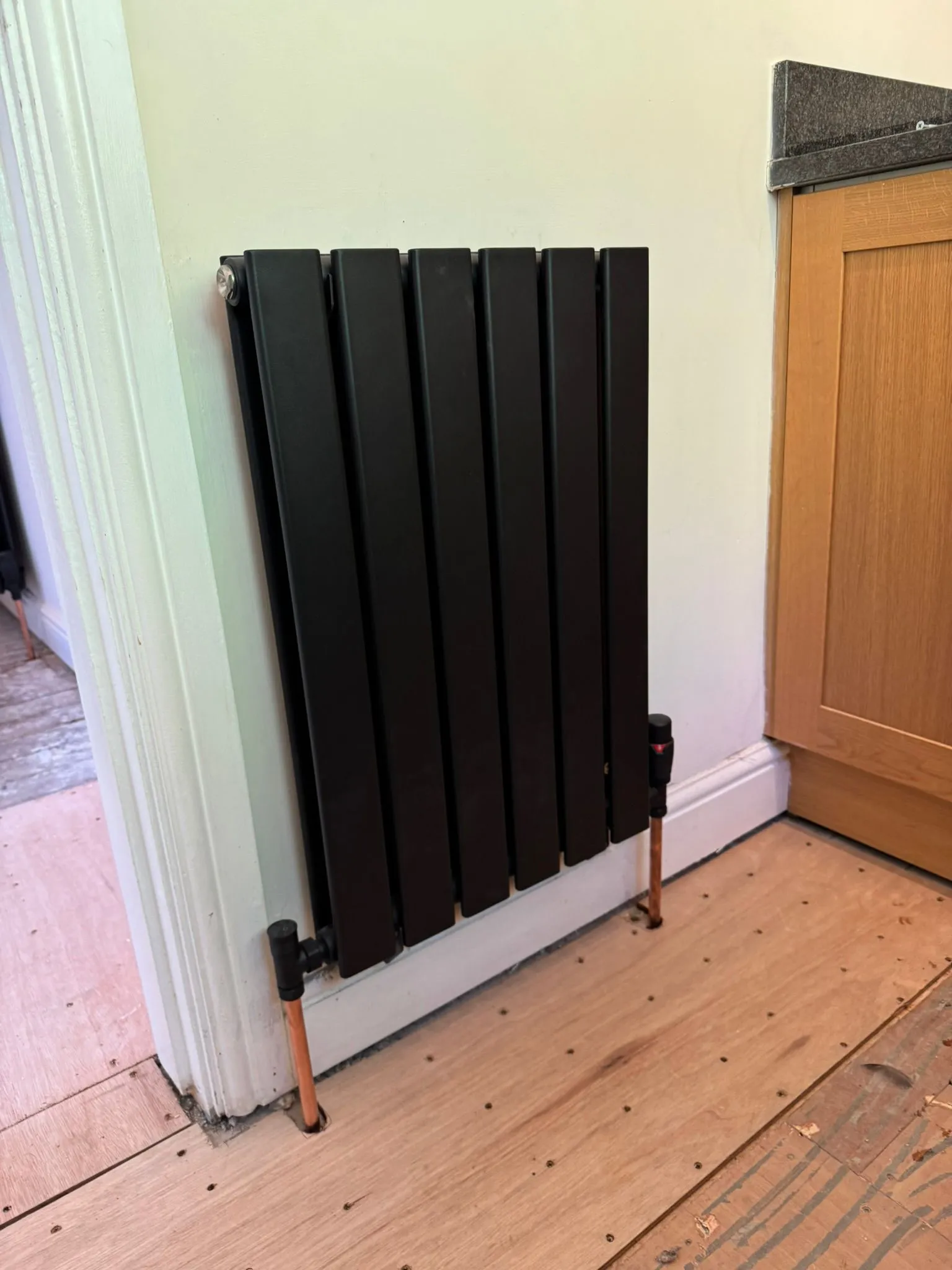 A modern black designer radiator with copper piping installed by Redorr Heating & Cooling Services Ltd.