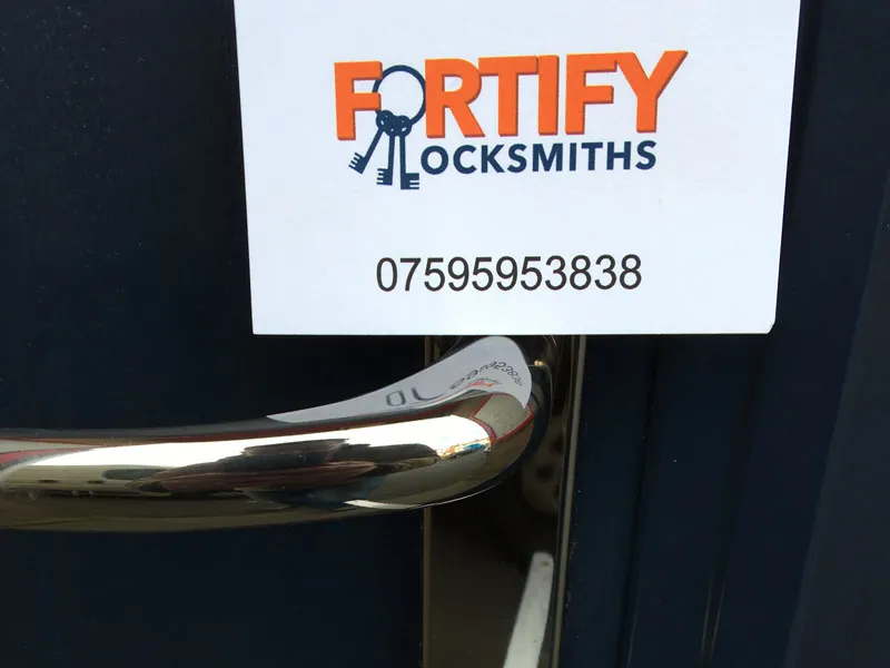 Fortify Locksmiths business card and phone number above a door handle
