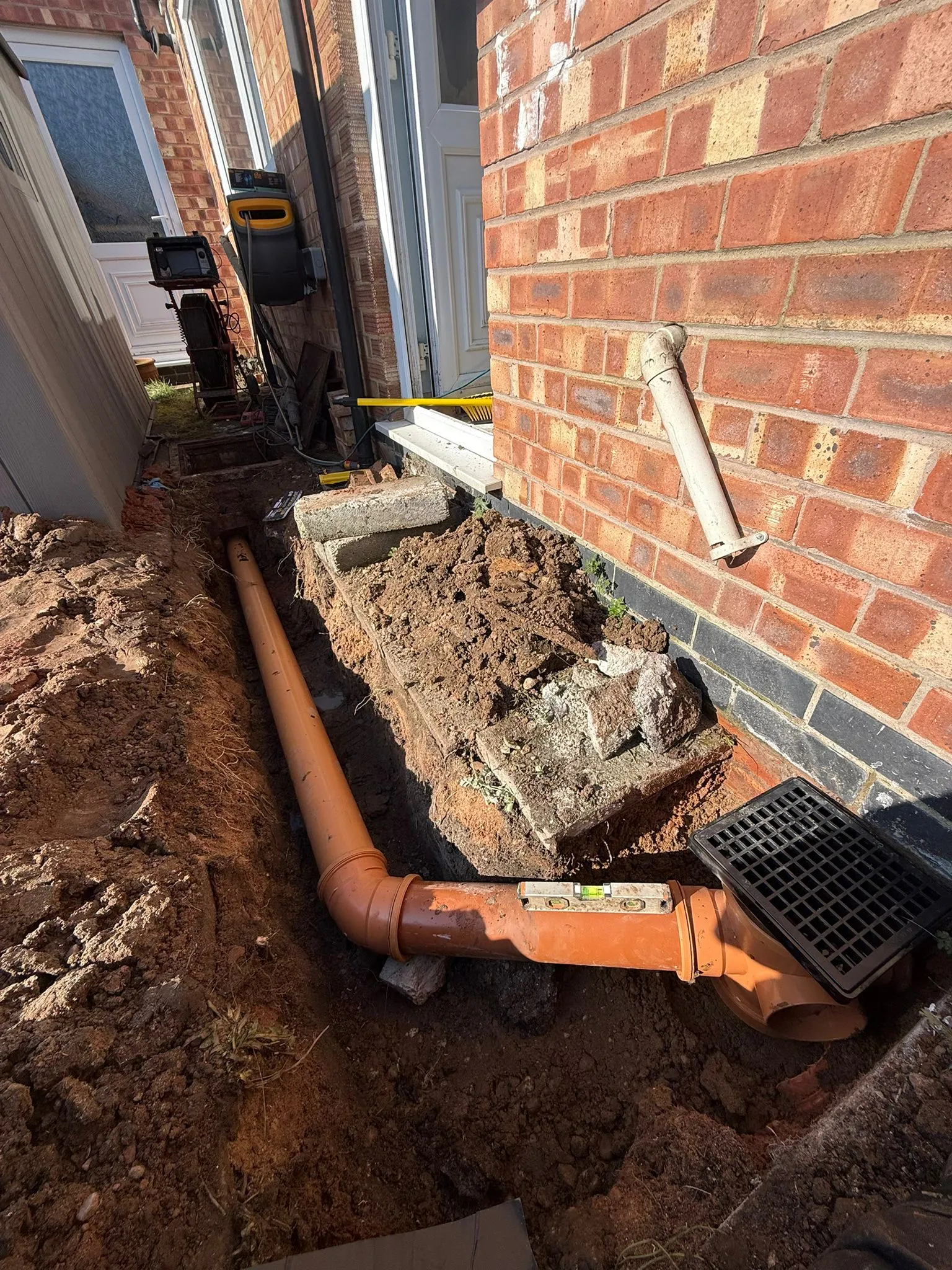 New underground drainage pipes and a gully being installed in a trench with a spirit level and professional CCTV drain survey equipment in the background.